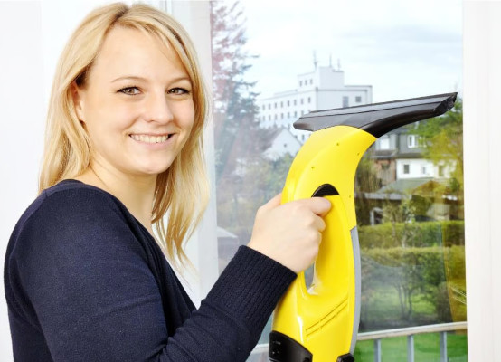 Frau reinigt Fenster mit Fensterrauger